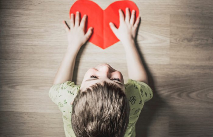Bērns uz grīdas tur papīra sirdi | Cilmes šūnu banku alianse | LYL BioBank Hearts
